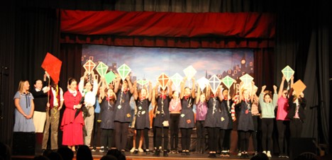 large group of students on stage with kites